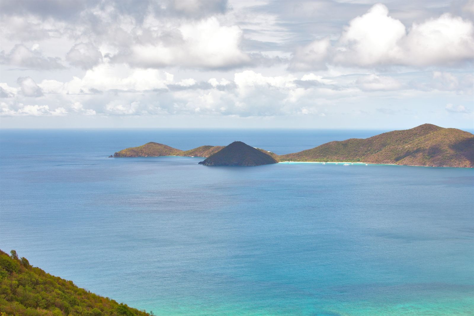 Calm blue sea and small islands seen from a hillside in the Virgin Islands under scattered clouds