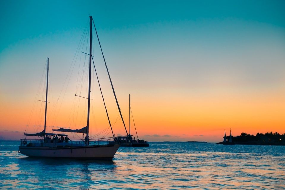 Sailboat silhouetted against an orange Caribbean sunset